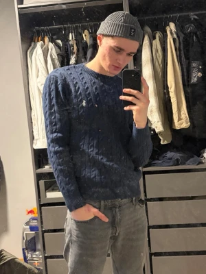 Mörkblå stickad tröja från Polo Ralph Lauren - Säljer en klassisk mörkblå kabelstickad tröja från Polo Ralph Lauren. Tröjan har rund halsringning, lång ärm och den ikoniska vita broderade loggan på bröstet. Perfekt för lager-på-lager och riktigt skön att bära under kyliga dagar.