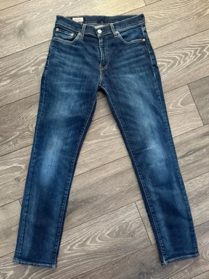 Levi's 511 blå jeans W29 L32 - Säljer ett par klassiska Levi's 511 jeans i mörkblå tvätt. Modellen har smal passform, fem fickor och snygga kontrastsömmar. Tillverkade i slitstarkt bomullsjeansmaterial med en liten stretch för extra komfort. Perfekta till sneakers eller boots. Liten reva längst nere på baksidan av vänster benet.