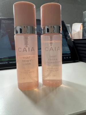 CAIA Setting Spray Duo - Två CAIA setting sprays i snygga rosa flaskor med silverdetaljer. Ena är 'That Dewy Look' för glow och den andra 'That Extra Hydration' för extra fukt. Perfekta för att fixera sminket och ge huden en fräsch finish.