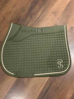 Olivgrön PS of Sweden schabrak💚 - Säljer ett olivgrönt schabrak från PS of Sweden med quiltad design och ljus kant. Broderad logga i hörnet och stilren look som passar perfekt till ridning. Materialet är mjukt och slitstarkt, och schabraket har en klassisk form. Bara använt 1 gång då jag skulle se om jag gilla färgen på min medryttarponny men de gjorde den inte💚 finns inte kvar på hemsidan längre! Går att diskutera pris! Köparen står för frakten!