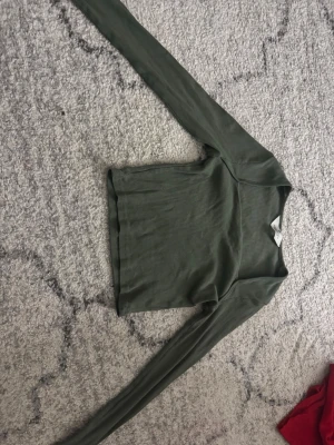 Olivgrön ribbad långärmad topp H&M - Säljer en olivgrön långärmad topp från H&M. Toppen har en croppad passform och är enkel men snygg att styla till olika outfits. Perfekt för dig som gillar basic men ändå vill ha något med lite edge. Använd endast en gång.