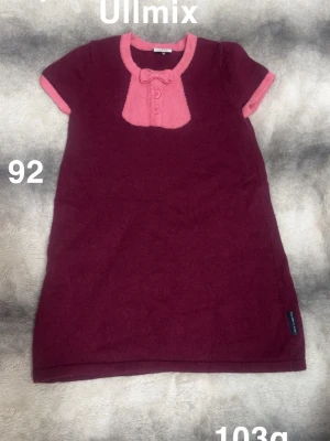 Vinröd ullmixklänning med rosett - Supersöt vinröd kortklänning från Polarn o pyret i ullmix med rosa detaljer, korta ärmar och en gullig rosett vid halsen. Knappslå framtill och kontrastfärgade kanter ger en extra touch. Perfekt för dig som gillar mjuka och bekväma plagg!🌸 Sparsamt använd. Storlek 92 