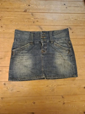 Blå jeansekjol - En supersnygg jeanskjol i 2000-talsstil. Den är från Lindex och är i stl 40, men jag skulle säga att den passar även någon som har stl 38 då den är lite mindre i storleken. Ena fickan hade lossnat lite i sömmen, men jag har sytt ihop den nu, så den är hel (bild 3).