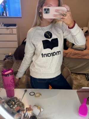 Grå isabel Marant sweatshirt - Säljer en grå sweatshirt från Isabel Marant med stort svart logotryck framtill. Tröjan har rund hals, långa ärmar och ribbade muddar vid ärmslut och nederkant. Perfekt för en chill och snygg look.
