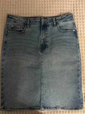 Ljusblå jeanskjol med fickor - Säljer en ljusblå jeanskjol med fem fickor, bälteshällor och rak passform. Kjolen har en enkel design utan mönster. 