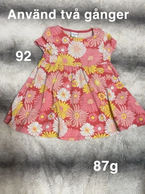 Blommig kortklänning  - Supersöt kortklänning med stora blommor i rosa, gul och vit på en rosa botten. Klänningen har korta ärmar och rund hals. Perfekt för sommarens alla äventyr  som känns skön mot huden.🌸 Använd två gånger. Storlek 92