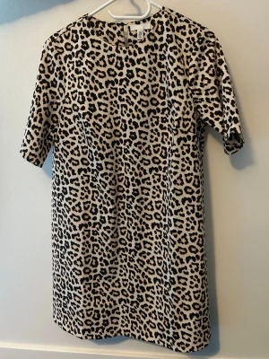 Leopardmönstrad kortklänning H&M - Säljer en kort klänning från H&M med leopardmönster i beige, svart och bruna toner. Klänningen har rak passform, korta ärmar och rund halsringning. Perfekt för dig som vill sticka ut med ett djurmönster.