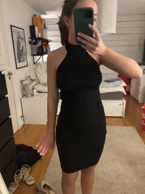 Svart tight halterneck klänning - Säljer en svart, tight halterneck klänning med öppen rygg och kort längd. Klänningen har en stilren och enkel design som framhäver figuren och är perfekt för dig som gillar minimalistisk stil. Materialet känns stretchigt och bekvämt.