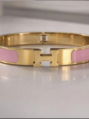 H-armband - Säljer ikoniska H-armband i guldpläterad metall med emaljdetaljer. Finns i svart, vit, röd, rosa, gråblå och orange. Snyggt H-spänne framtill och stilren design som lyfter din outfit. Perfekt accessoar för dig som gillar lyx och färg.