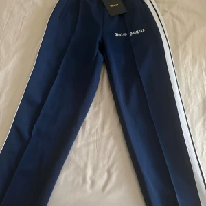 Palm Angels  - Säljer marinblå Palm Angels-byxor i mycket fint skick. Endast använda två gånger. Hög kvalitet och stilren Palm Angels-design, perfekt för en clean streetwear-look. Vid intresse eller frågor är det bara att skriva. Skickas snabbt vid köp.
