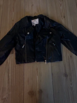 Svart skinnjacka från Mywear Young - Säljer en svart skinnjacka från Mywear Young i storlek 122/128. Jackan har klassisk bikerstil med snedställda dragkedjor, bred krage och silverfärgade detaljer. Perfekt för dig som vill ha en cool och tidlös look.