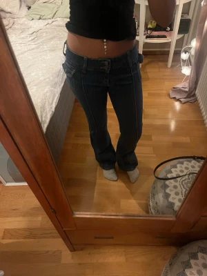Mörkblå lågmidjade jeans - Säljer ett par supersnygga mörkblå lågmidjade jeans med bootcut från brandy Melville. Knappen på ena framfickan är dock av som man ser på sista bilden, annars är de i jätte bra skick 