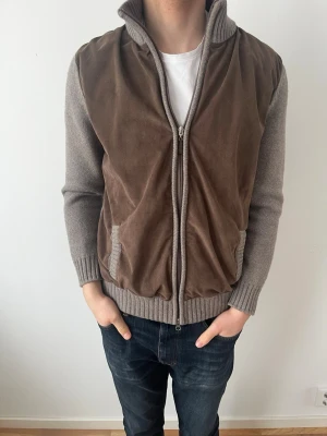 Gran Sasso brun och grå cardigan jacka - Snygg cardigan jacka från Gran Sasso i grått och brunt, med stickade muddar och krage. Framsidan och armbågarna har mockadetaljer, och jackan har dragkedja hela vägen. Tillverkad i Italien, perfekt för dig som gillar klassisk stil med en twist.