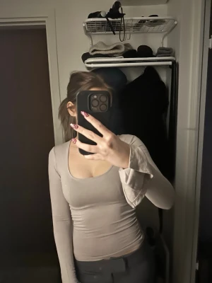 Beige långärmad topp med trumpetärm - Säljer en beige långärmad topp med figurnära passform och trumpetärmar. Toppen har en rundad, djup urringning och är tillverkad i ett mjukt stretchigt material som sitter snyggt på kroppen. Perfekt att styla med jeans eller kjol.