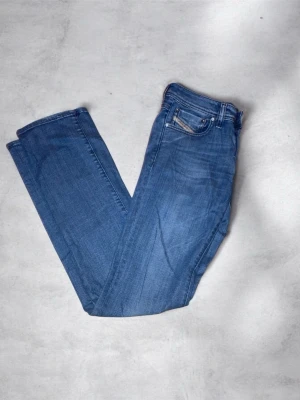 Blå Diesel jeans straight fit - Säljer ett par klassiska blå jeans från Diesel med raka ben och normal passform. Jeansen har fem fickor, snygga sömmar och diskret Diesel Industry-märke på fickan. Tillverkade i slitstarkt bomullsjeansmaterial. Perfekta till sneakers eller boots.