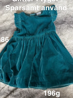 Turkos glittrig sammetsklänning - Supersöt turkos klänning i sammetsmaterial med glittriga detaljer. Klänningen har volangärmar och en utställd kjol som ger en gullig look. Perfekt för dig som vill sticka ut lite extra!🌸 Sparsamt använd. Glitter i tyget. Storlek 86.