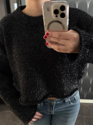 Glittrig svart fluffig tröja - Säljer en svart fluffig tröja med glittriga inslag. Tröjan har en loose, lite croppad passform och långa ärmar, perfekt för dig som vill ha något mysigt men ändå lite extra.  Den har långa snygga ärmar💕