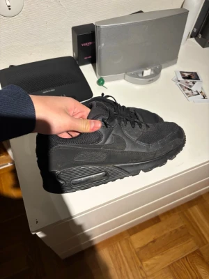 Nike Air Max 90 Triple Black sneakers - Säljer ett par helsvarta Nike Air Max 90 sneakers med klassisk chunky sula och synlig Air-enhet. Skorna har mesh och syntet på ovandelen, samt snörning för perfekt passform. Perfekta för dig som gillar en clean och sportig look. PRISET KAN PRUTAS NER OCH KAN ÄVEN FOTA SKORNA TILL ER SOM ÄR INTRESSERADE