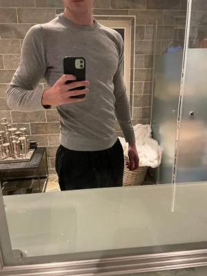 Grå slim fit tröja Lindbergh - Slimmad grå tröja från Lindbergh i mjuk merinoull. Modellen har rund hals och långa ärmar, perfekt för dig som gillar en stilren och enkel look. Passformen är slim fit och materialet känns lyxigt och skönt mot huden.