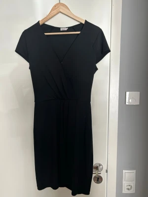 Svart omlottklänning från Filippa K - Stilren svart omlottklänning från Filippa K i storlek M. Klänningen har v-ringning, korta ärmar och en smickrande passform som markerar midjan. I jättebra skick.