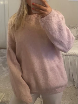 Ljusrosa stickad tröja - Mysig ljusrosa stickad tröja med oversized passform och långa ärmar. Perfekt för kyliga dagar och enkel att matcha med både jeans och mjukisbyxor. Tröjan har en rund halsringning och är supermjuk.