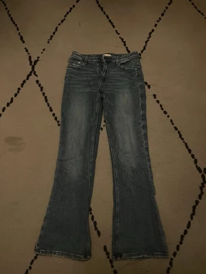 Blå bootcut jeans Gina Tricot 164 - Bootcut jeans från Gina Tricot i klassisk blå tvätt. Jeansen har fem fickor, knapp och dragkedja framtill samt en snygg utsvängd passform nertill. Tillverkade i mjukt denimtyg som sitter skönt på kroppen. Syn på andvändning längst ner vid hälen men inget stort
