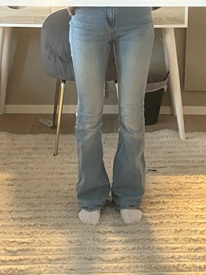 Ljusblå bootcut jeans med hög midja - Säljer ett par ljusblå jeans med bootcut-modell och hög midja. Jeansen har klassiska fem fickor, dragkedja och knapp framtill samt snyggt utsvängda ben. Perfekta till sneakers eller boots och tillverkade i mjukt denimtyg.