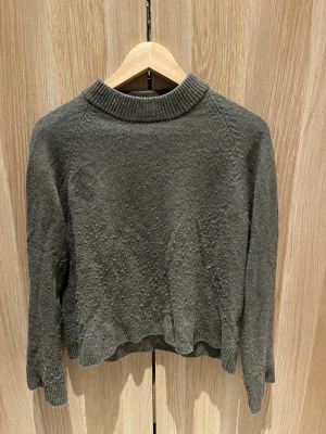 Mörkgrå stickad tröja från Wera - Mysig mörkgrå stickad tröja från Wera med ribbad krage och långa ärmar. Perfekt till höst och vinter när du vill ha något enkelt men ändå snyggt. Passar dig som gillar en klassisk och clean look.