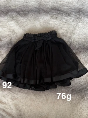 Pompdelux kjol - Supersöt svart kortkjol med flera lager tyll och bred volangkant. Kjolen har en fin rosett i midjan och elastisk resår för skön passform. Perfekt för dig som gillar en lekfull och fluffig stil.🌸Sparsam använd. Storlek 92 