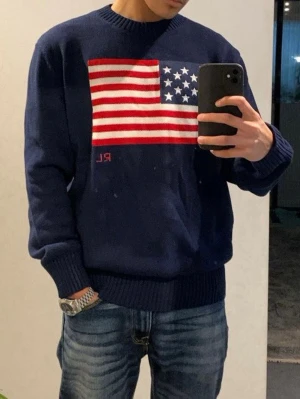 Blå stickad tröja Polo Ralph Lauren - Säljer en mörkblå stickad tröja från Polo Ralph Lauren med amerikansk flagga på bröstet och RL-broderi. Tröjan har rund halsringning, ribbade muddar och är långärmad. Perfekt för dig som vill ha en klassisk college-look.