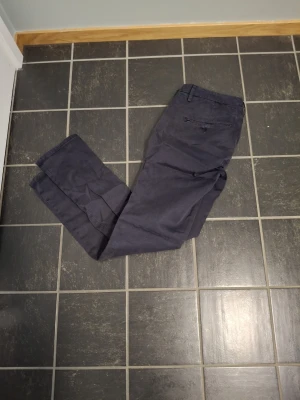 Mörkblå chinos från Dondup, strl 33 - Säljer ett par mörkblå chinos från Dondup i storlek 33. Byxorna har raka ben, bälteshällor och klassiska fickor både fram och bak. Materialet är mjukt och skönt, perfekt för en clean och stilren look.