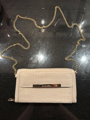 Beige axelväska - Jag säljer en beige axelväska/crossbody väska med guldiga detaljer från märket AMISU i mycket gott skick!