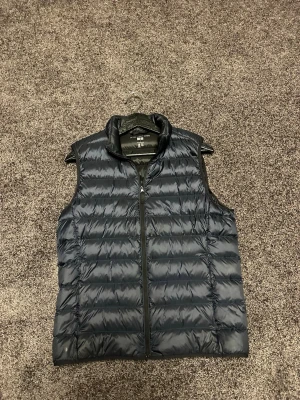 Uniqlo väst - Säljer en svart, dunväst från Uniqlo Ultra Light Down. Västen har hög krage och dragkedja framtill. Perfekt att slänga över en hoodie eller tröja när det är kyligt ute. Enkel och stilren design som funkar till det mesta.