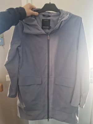 Ljusgrå/lila regnjacka från Didriksons - Säljer en snygg ljusgrå/lila regnjacka/regnkappa från Didriksons med huva och stora fickor framtill. Jackan är 100% vattentät och har dragkedja hela vägen upp. Perfekt för blöta dagar och har en clean, enkel look. Har blivit lite solblekt, men ingenting som påverkar funktionen.