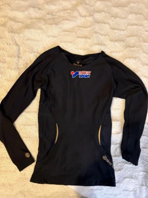 Svart långärmad träningströja  - Svart långärmad träningströja från InterSport i storlek M (passar mig som vanligtvis har XS). Tröjan har Intersport-logga på bröstet, guldfärgade detaljer och mönster på ryggen samt diskreta loggor på ärmarna. Tillverkad i syntetmaterial som andas, perfekt för sport och träning.