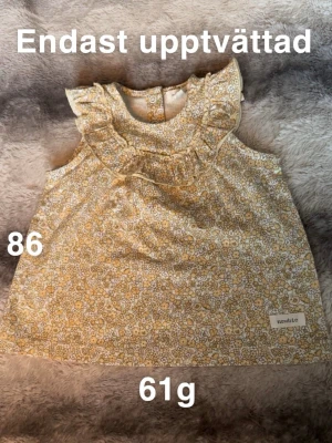 Blommig ärmlös blus från Newbie - Söt blommig blus från Newbie i storlek 86. Blusen är ärmlös med volangdetaljer vid axlar och halsringning. Färgen är ljusgul med små blommor över hela plagget. Perfekt för vår och sommar!🌸Oanvänd. Endast upptvättad. Storlek 86