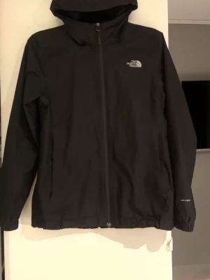 Svart vindjacka från The North Face - Säljer en svart vindjacka från The North Face, passar både tjejer och killar, dock i tjejmodell. Använd en gång, alltså som ny