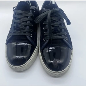 Lanvin sneakers i mocka och lack - Snygga mörkblå sneakers från Lanvin med ovandel i mocka och lackad tå. Skorna har rund tå, platt vit sula och klassisk snörning. Kommer med original dustbag. Perfekta för dig som gillar exklusiva och stilrena sneakers med unika materialval.