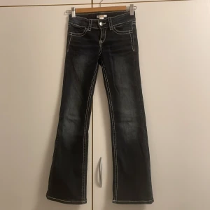 Bootcut jeans med broderade fickor - Snygga mörkblå bootcut jeans från Gina Tricot med kontrasterande vita sömmar och broderade bakfickor med beige mönster och små paljetter. Jeansen har klassisk femficksdesign, knappstängning och är tillverkade i jeansmaterial.