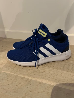 Blå adidas sneakers med vita ränder - Snygga blå sneakers från adidas med klassiska vita ränder på sidorna och vit sula. Skorna har snörning, mesh-ovandel och gula detaljer vid öglorna och loggan på plösen. Perfekt för dig som gillar sportig stil och vill ha bekväma skor till vardagen. Ena skon är 37,1/3och den andra 38 men passar både en 37,1/3 eller 38. 