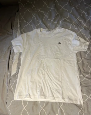Vit Lacoste t-shirt regular fit - Vit t-shirt från Lacoste i regular fit med klassisk krokodillogga broderad på bröstet. T-shirten har rund hals och korta ärmar, tillverkad i mjuk bomull som känns skön mot huden. Enkel och stilren design som funkar till allt.
