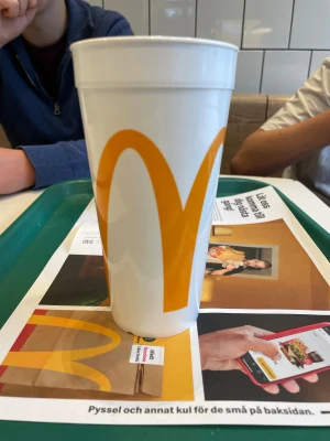 McDonald's vit plastmugg 0,5L - Stor vit plastmugg från McDonald's med den klassiska gula M-loggan och röd Coca-Cola-märkning. Muggen rymmer 0,5 liter och har en rund, hög form som passar perfekt för läsk eller annan dryck. Snygg att ha med sig på språng eller som samlarpryl. Gjord 1954