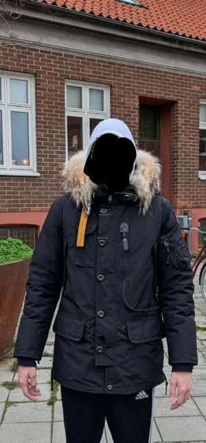 Svart Parajumpers parkajacka M kodiak  - Säljer en svart Parajumpers kodiak parkajacka i storlek medium. Jackan har päls på huvan, flera fickor med knappar och dragkedja, samt den klassiska gula remmen vid kragen. Materialet är polyester och jackan är quiltad för extra värme.