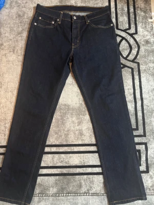 Levi's 511 mörkblå jeans W33 L32 - Snygga Levi's 511 jeans i mörkblå tvätt med klassiska kontrastsömmar och fem fickor. Modellen har en slim passform och raka ben, perfekt för dig som gillar en modern och stilren look. Jeansen är tillverkade i slitstarkt denim och har den ikoniska Levi's-lappen bak.