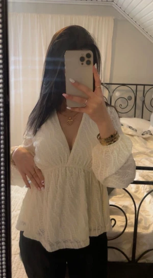 Vit blus med v-ringning och volang - Säljer en vit blus med v-ringad hals och volang nedtill. Blusen har långärmade puffärmar och ett diskret mönster i tyget som ger en cool struktur. 