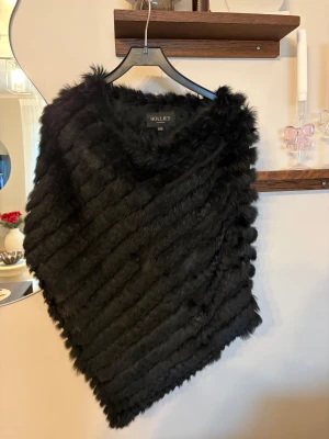 Svart pälsponcho från Hollies - Säljer en svart pälsponcho från Hollies med snyggt snedrandigt mönster.