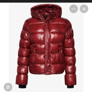Röd pufferjacka med huva från Superdry - Säljer en riktigt snygg röd pufferjacka från Superdry med glansig finish och huva. Jackan har dragkedja, knappar och två stora fickor framtill. Den är quiltad och har svarta muddar vid ärmslut. Perfekt för dig som vill ha en varm och trendig look. Stl M dvs 38 men passar även om man som mig vanligtvis har S