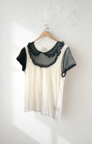 Vit blus med svart spets från RED Valentino - Supersöt vit blus från RED Valentino med svarta, korta ärmar i transparent spets och prickigt mönster. Kragen har volangdetaljer i samma svarta spets som ger en extra cool touch. Perfekt för dig som gillar unika detaljer och vill sticka ut lite extra.   Se bilder för skick och eventuella fläckar eller slitningar.  Rökfritt och djurfritt hem!