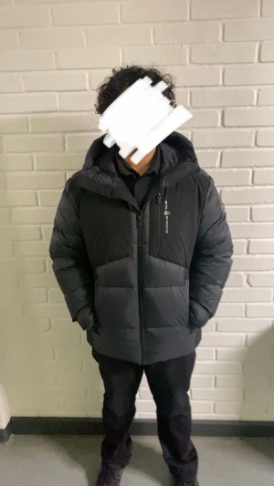 Svart Sail Racing jacka herr XL - Svart dunjacka från Sail Racing med huva och dragkedja framtill. Jackan har en clean look med logga på bröstet och ärmen, samt praktiska fickor. Perfekt för kalla dagar speciellt just nu. har aldrig ägt en varmare jacka, säljer den för den är för stor. Har haft den i ett par veckor, storlek XL finns i Lessebo/växjö