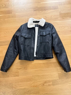 Svart teddyjacka från FB Sister XS - Väldigt fin, Svart teddyjacka från FB Sister i storlek XS. Jackan har en mjuk, beige teddykrage och hel teddyfoder på insidan. Yttermaterialet är skinnimitation med två stora bröstfickor och knappar framtill. Croppad passform och långa ärmar ger en fin look. Köpt för 500. Säljer för 300. 